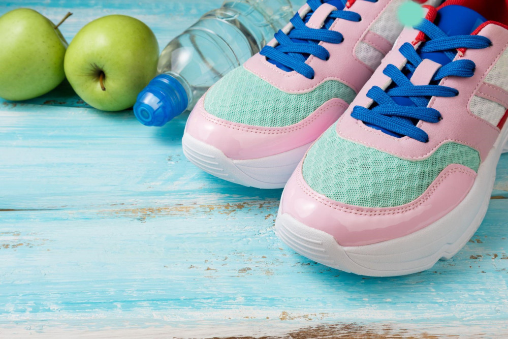 różowe buty sportowe, butelka wody i jabłka
