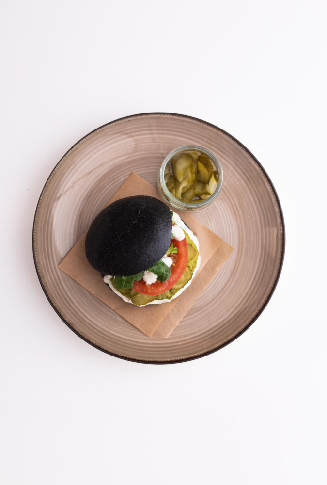 Burger z zielonego groszku w czarnej bułce z warzywami i sosem majonezowo-jogurtowym